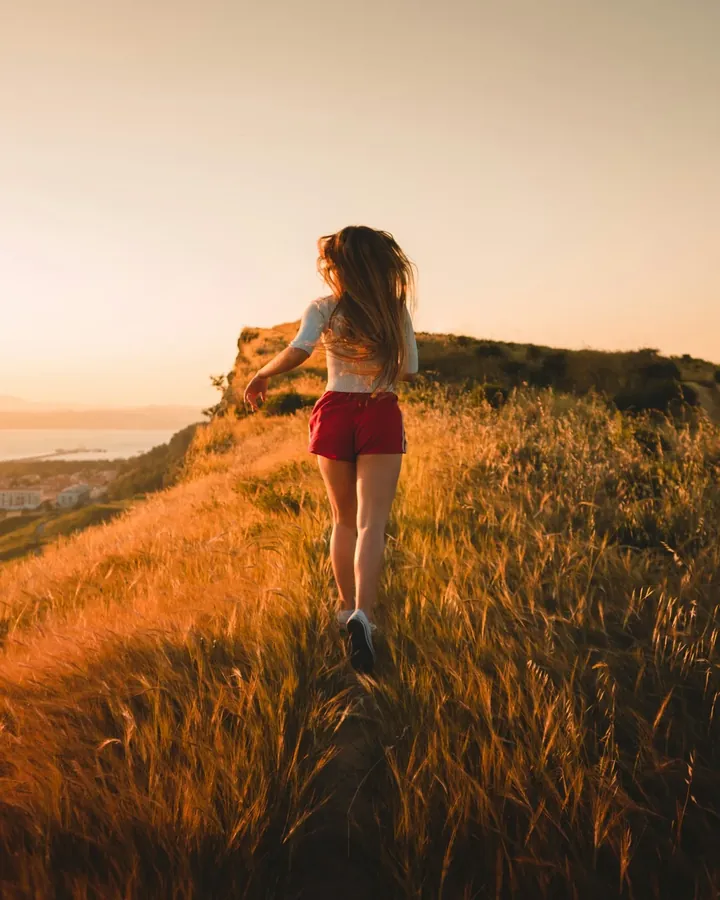 Une femme court dans les herbes hautes au coucher du soleil