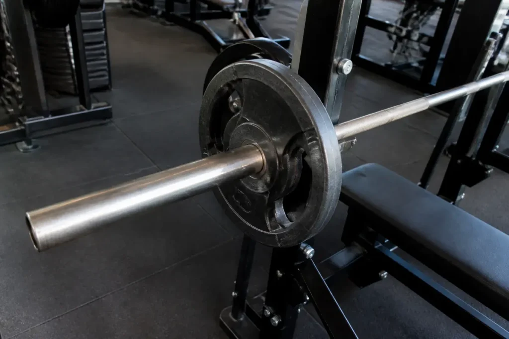 Barre d'haltérophilie avec disques noirs sur banc de musculation dans une salle de sport.